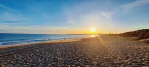A beach with a sunset, sandy shore, and a few people walking.