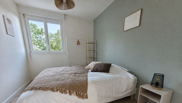 A bedroom with a bed, a bedside table, a window, and a wall-mounted ladder. - Renovated Apartment in Quimper – 3 Bedrooms – Sleeps 6 (Quimper)