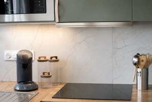 A modern kitchen with a coffee maker, two glass containers, a metal utensil holder, and a black induction cooktop. - Renovated Apartment in Quimper – 3 Bedrooms – Sleeps 6 (Quimper)
