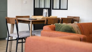 A modern living room with a wooden dining table, grey cushioned chairs, and a red sofa with a throw blanket. - Renovated Apartment in Quimper – 3 Bedrooms – Sleeps 6 (Quimper)