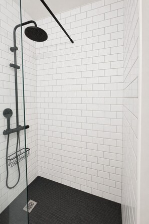 A shower area with white tiled walls and a black floor. - Renovated Apartment in Quimper – 3 Bedrooms – Sleeps 6 (Quimper)