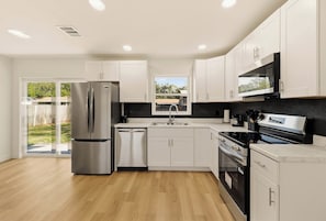 A modern kitchen with white cabinetry, stainless steel appliances, and a black countertop backsplash.
