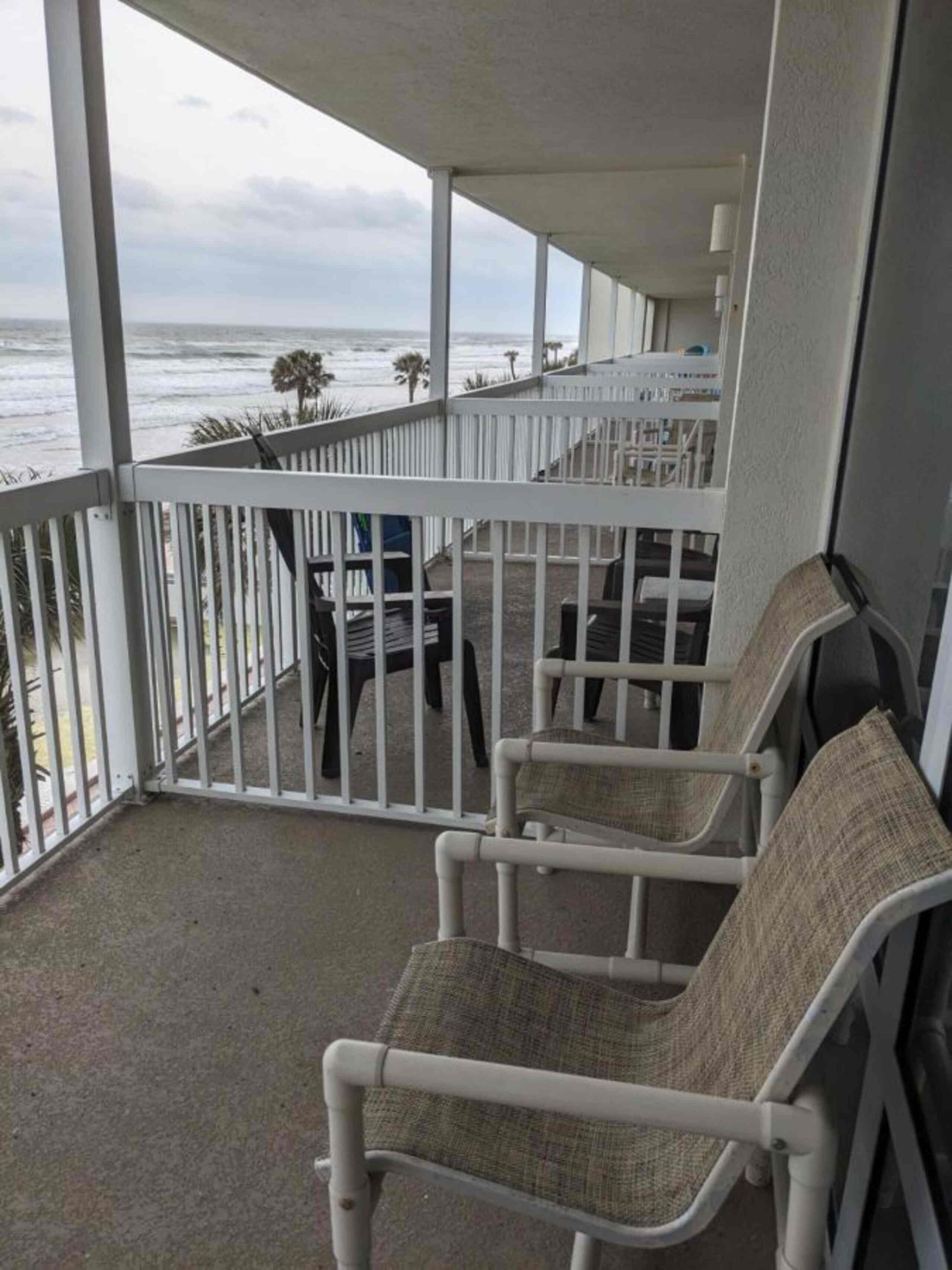 A balcony with white railings, two wicker chairs, and a view of the ocean.