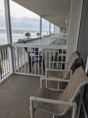 Ein Balkon mit weißen Geländern, zwei Korbstühlen und Blick aufs Meer.