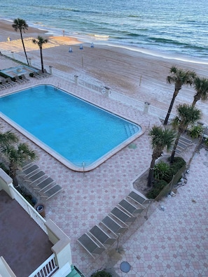 Ein Schwimmbecken neben einem Strand mit Palmen und Liegestühlen.