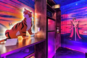 Ein Zimmer mit Wandgemälde von einem Tiger und einer Hexe, einer Tür und einer violett beleuchteten Wand.