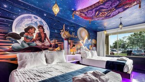 Ein Zimmer mit einem großen Bett, einem kleinen Sofa und einem Nachttisch. An der Wand befindet sich ein Wandgemälde, das eine Szene mit zwei Personen und einem Halbmond zeigt.