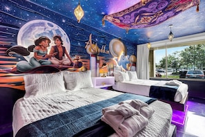 Ein Zimmer mit einem großen Bett, einem kleinen Sofa und einem Nachttisch. An der Wand befindet sich ein Wandgemälde, das eine Szene mit zwei Personen und einem Halbmond zeigt.