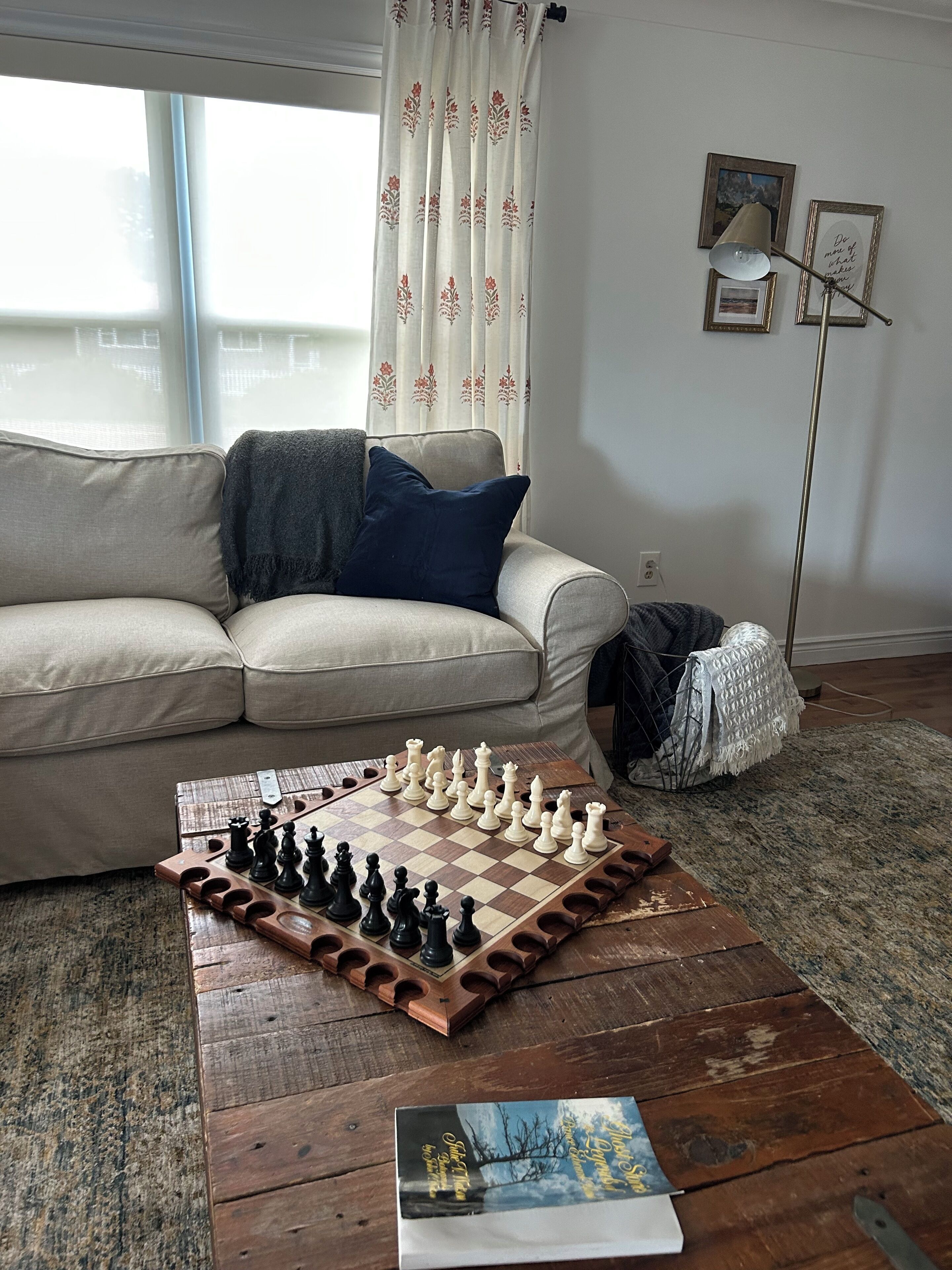 A living room with a chessboard on a wooden coffee table, a sofa with cushions, a blanket, and a lamp.