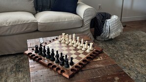 A living room with a chessboard on a wooden coffee table, a sofa with cushions, a blanket, and a lamp.