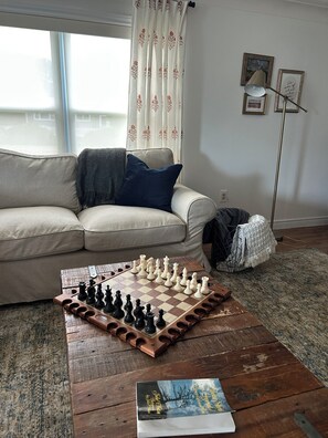 A living room with a chessboard on a wooden coffee table, a sofa with cushions, a blanket, and a lamp.