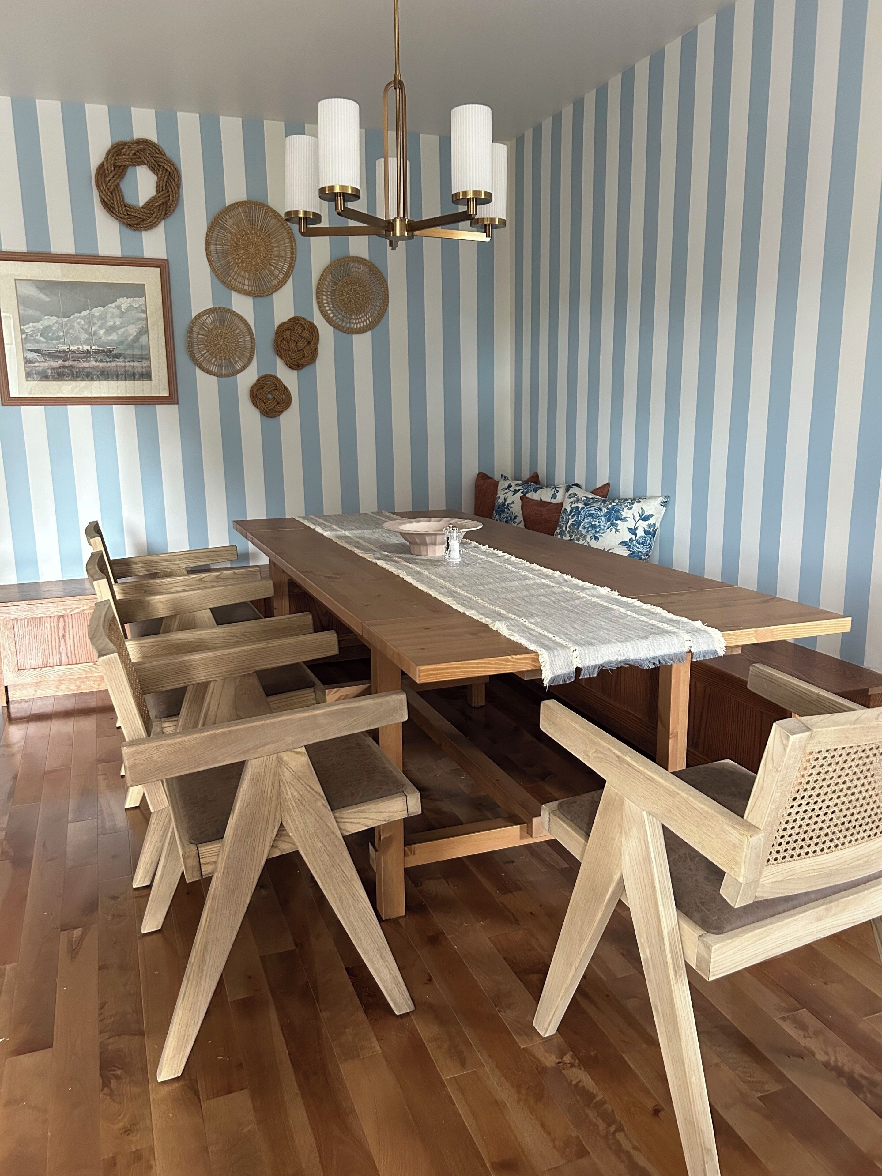 A dining area with a long wooden table, multiple chairs, a chandelier, and striped wallpaper.