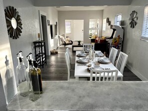 A dining area with a white table set for four, surrounded by white chairs. There are decorative wall clocks and a large mirror on the walls. - Lovely Home in Little Havana- Near Loan Depot Park (Miami)