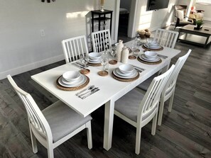 A dining table set with white plates, bowls, and cutlery, surrounded by white chairs with grey cushions. - Lovely Home in Little Havana- Near Loan Depot Park (Miami)