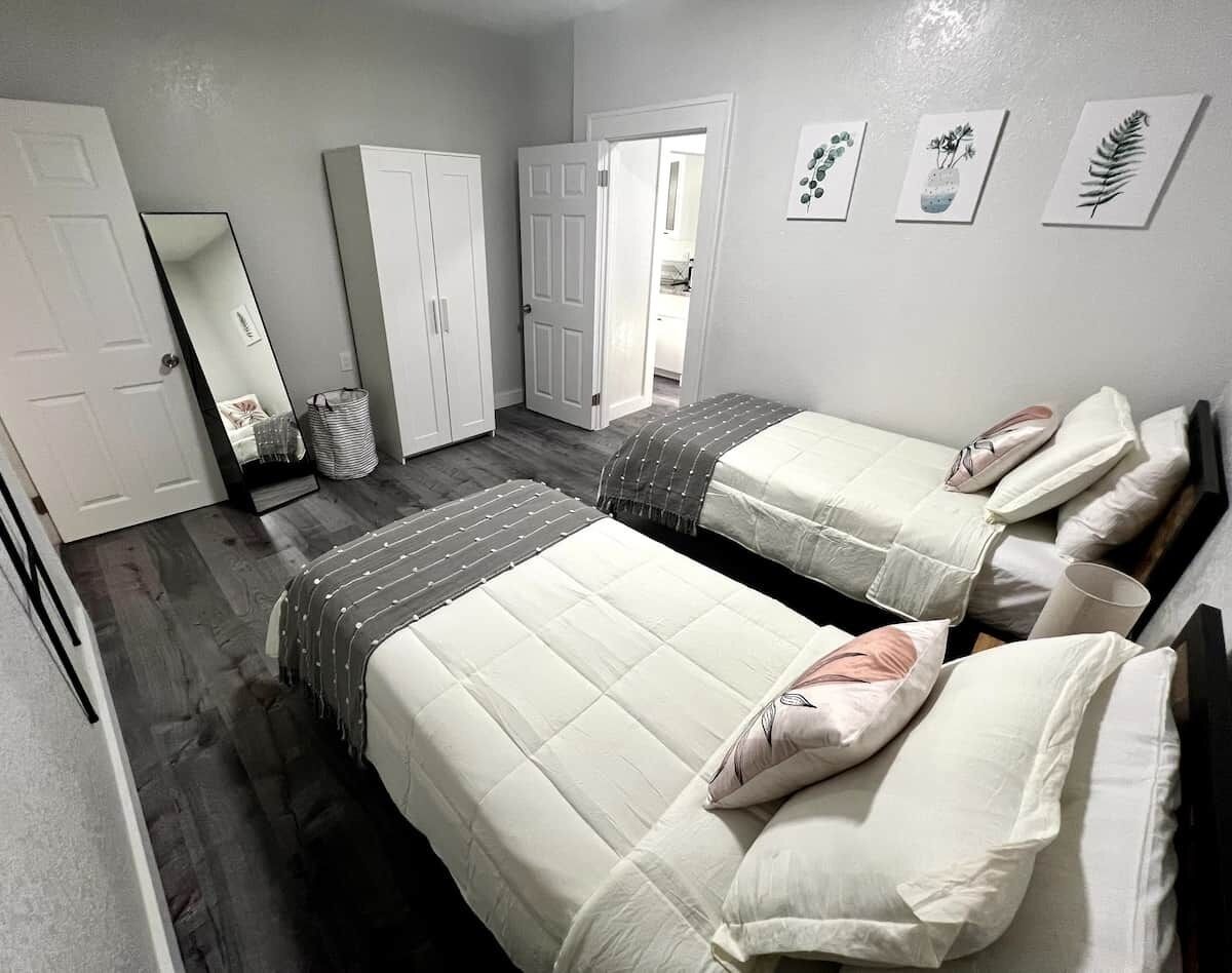 A bedroom with two beds, a wardrobe, a mirror, and a door leading to another room.