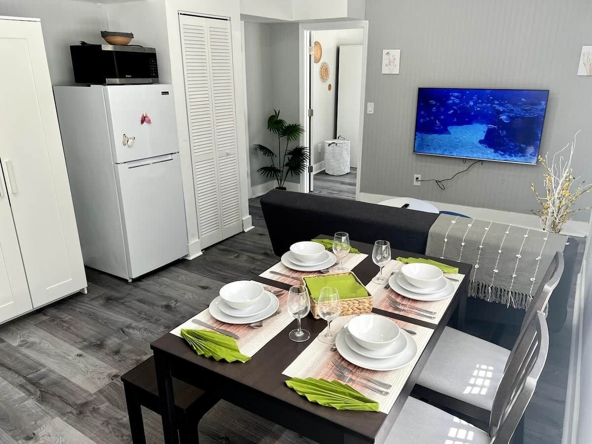 Ein Essbereich mit einem Tisch für vier Personen, einer Mikrowelle, einem Kühlschrank und einem an der Wand befestigten Fernseher.