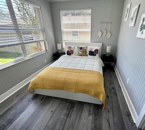 Ein Schlafzimmer mit einem Bett, zwei Nachttischen, einem Fenster und einer Wanddekoration.