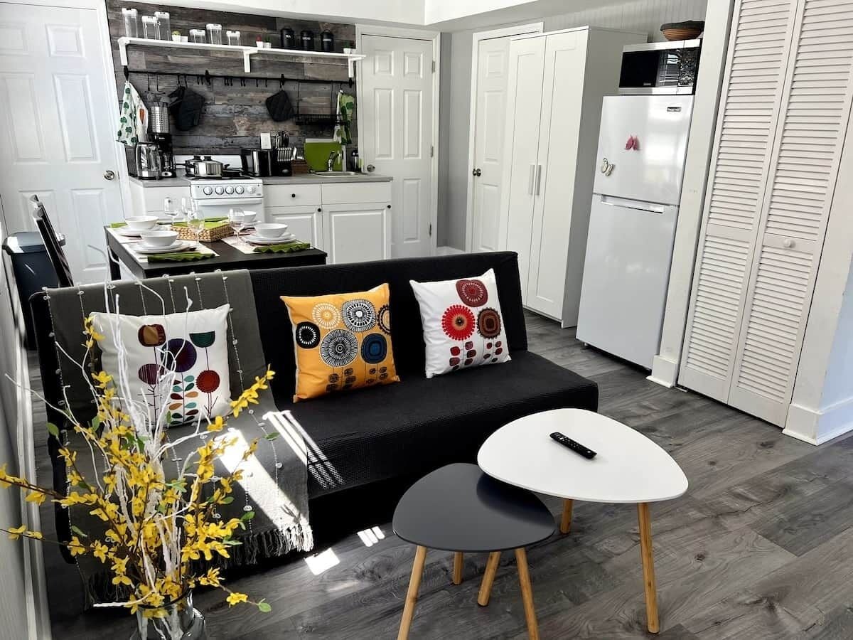 A compact living space with a sofa, two side tables, a small kitchen area, and a white refrigerator.