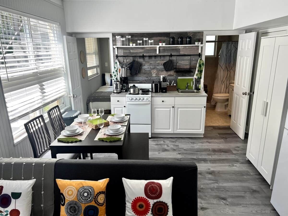 A compact kitchen with white cabinets, a dining area with a table set for four, and a view of the adjacent bathroom.