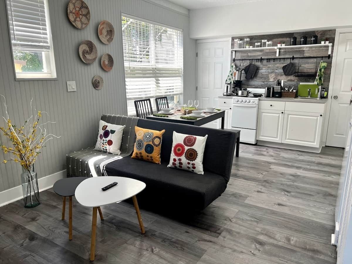 Una cocina moderna con gabinetes blancos, una estufa y un comedor con un sofá negro y una mesa pequeña.