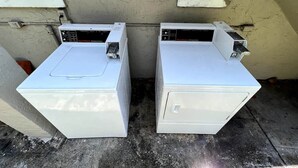 Dos electrodomèstics blancs, possiblement rentadores, col·locats a l'exterior davant d'una paret amb una finestra.