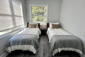 Ein Schlafzimmer mit zwei Betten, einem Fenster mit Jalousien und einem Nachttisch mit Lampe.