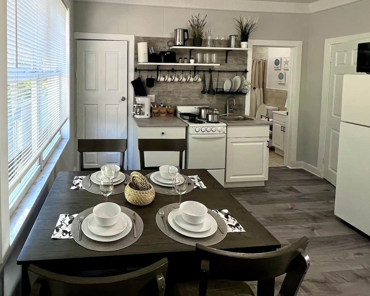 Une cuisine moderne avec des meubles blancs, une table à manger pour quatre personnes et un four encastré.