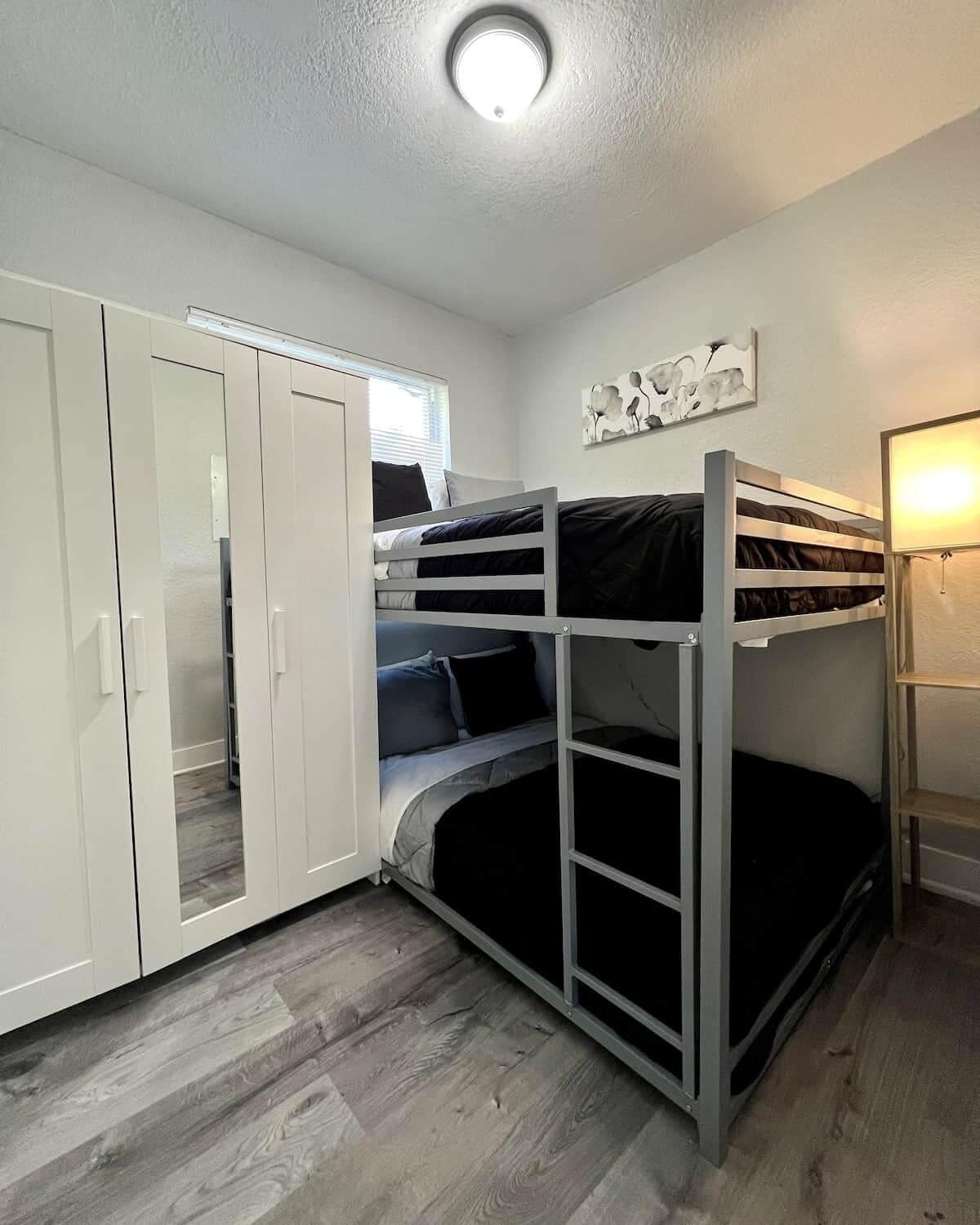 Ein Stockbett mit Schreibtisch und Kleiderschrank, eine Deckenleuchte und ein Wandbild.