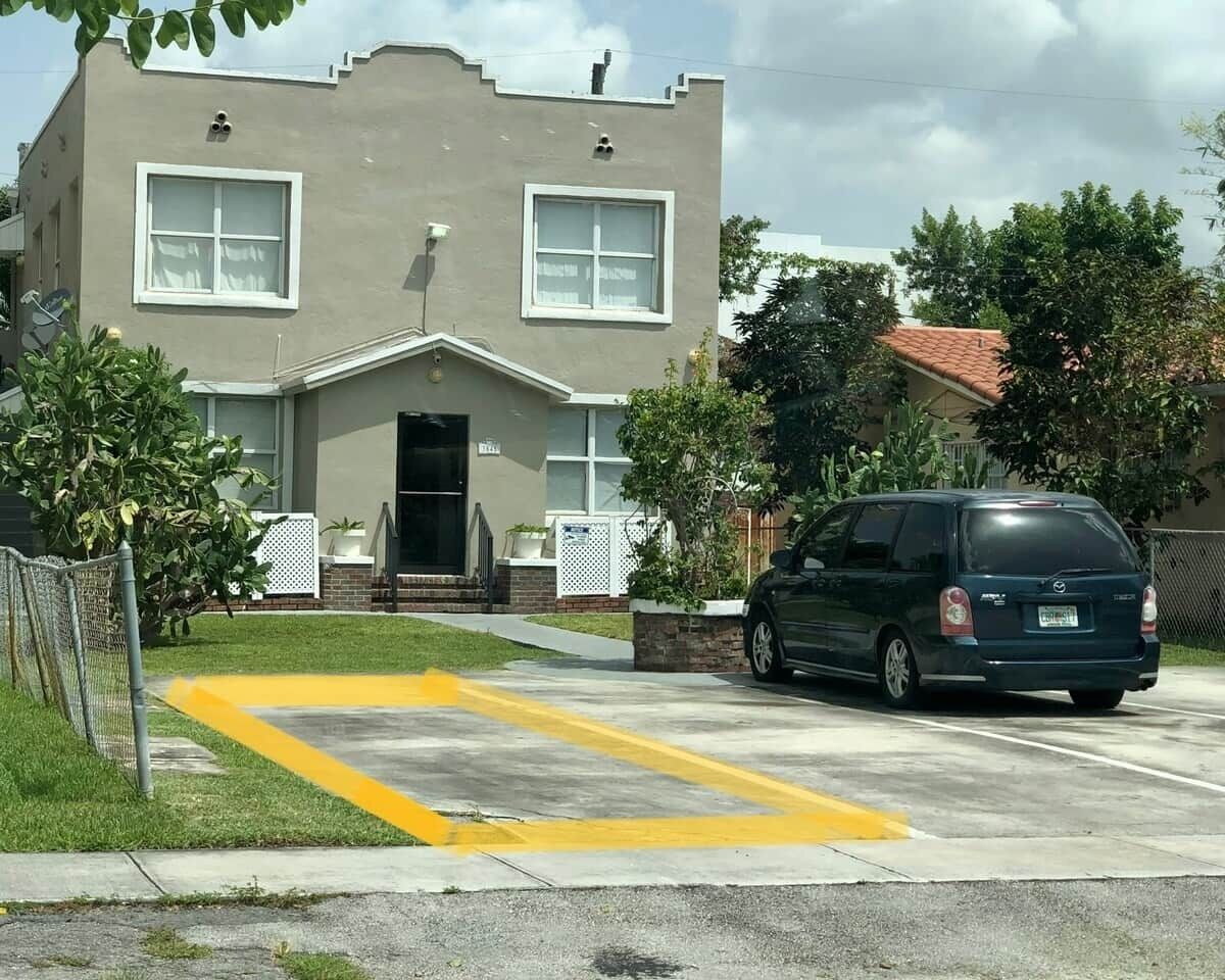 Ein zweistöckiges Gebäude mit Garage, einem geparkten Auto und einem gelben Stellplatz.