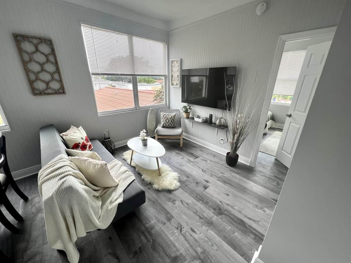Ein modernes Wohnzimmer mit einem grauen Sofa, einem runden Couchtisch und einem an der Wand befestigten Fernseher.