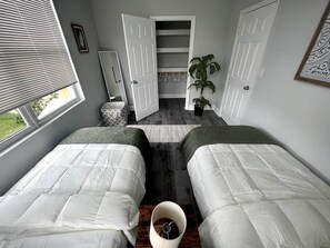 Een slaapkamer met twee bedden, een kast, een plant en een raam.