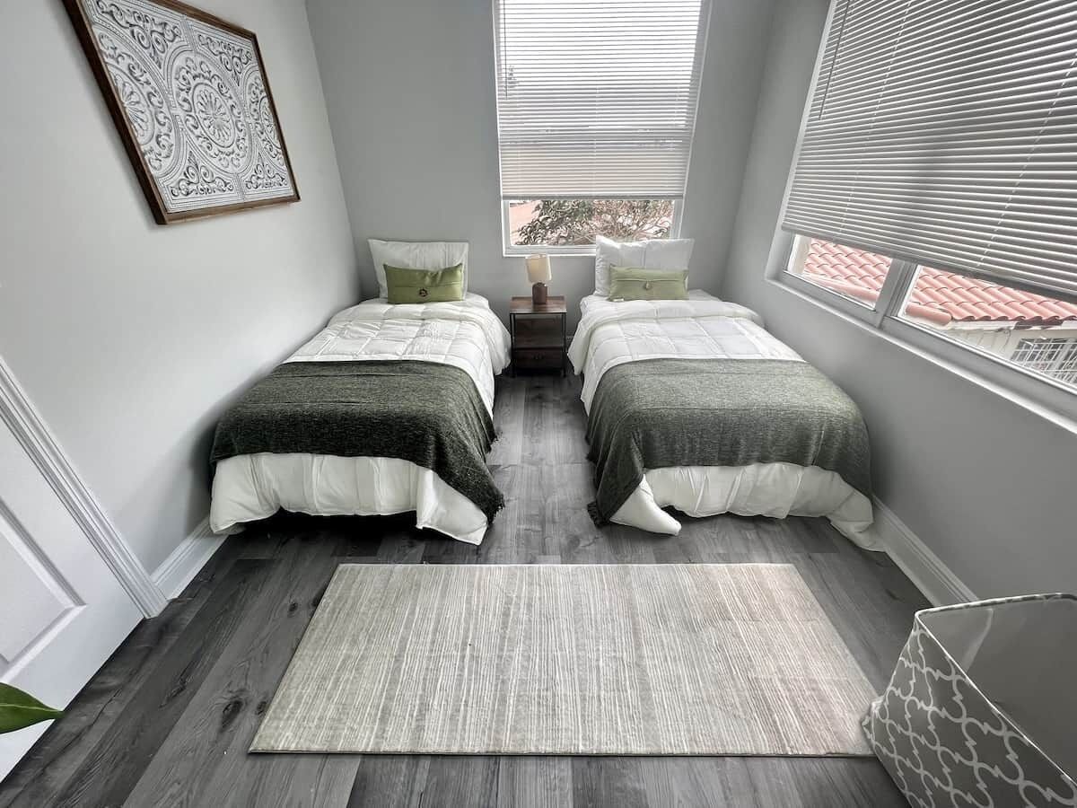 A bedroom with two beds, a rug, and a wall-mounted picture.
