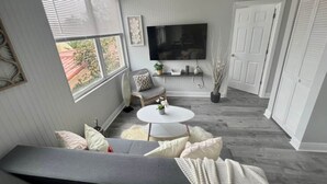 Ett vardagsrum med en grå soffa, ett vitt soffbord och en platt-TV som är monterad på väggen.
