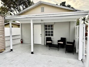 Eine überdachte Terrasse mit weißem Geländer, einem Feuerlöscher und zwei Stühlen.