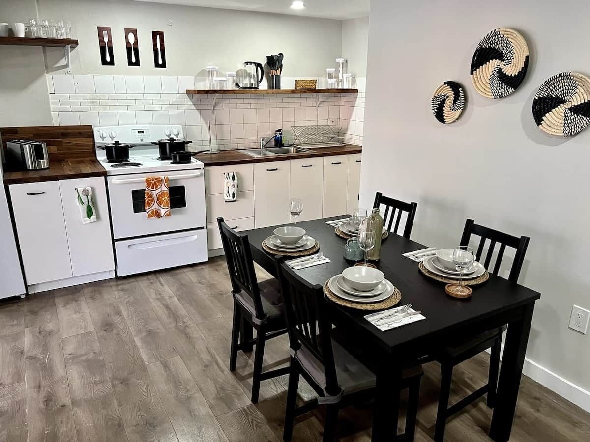 A modern kitchen with white cabinets, a black dining table set for four, and a small island with a stove.