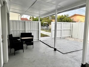Ein überdachter Patio-Bereich mit Betonboden, weißen Wänden und einem weißen Zaun.