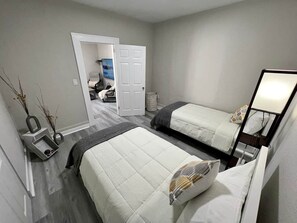 Un dormitorio con dos camas, una mesita de noche, un espejo y una puerta que da a otra habitación.