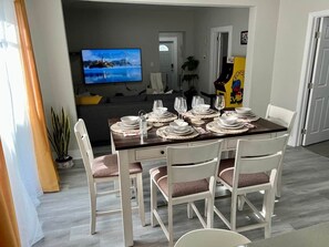 Ein Essbereich mit einem für vier Personen gedeckten Tisch, einem an der Wand montierten Fernseher und einer Pflanze in der Ecke.