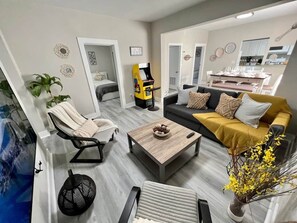 Una sala de estar moderna con un sofá, sillones, una mesa de centro y una consola de videojuegos.