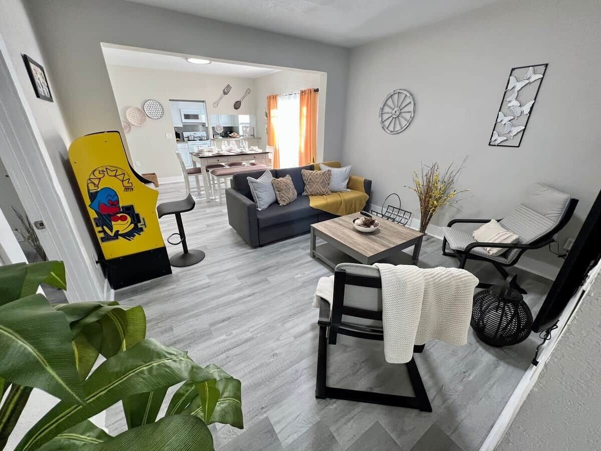A modern living room with a grey sofa, a coffee table, and a dining area in the background.