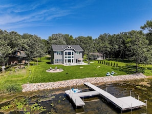 A two-story house with a large front yard, a dock, and a pond. - Lakefront 5BR on Rush Lake, Private Dock + Kayaks (New York Mills)