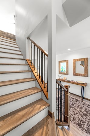 A staircase with wooden steps and metal railings, leading to a landing with a wooden bench and a mirror. - Lakefront 5BR on Rush Lake, Private Dock + Kayaks (New York Mills)
