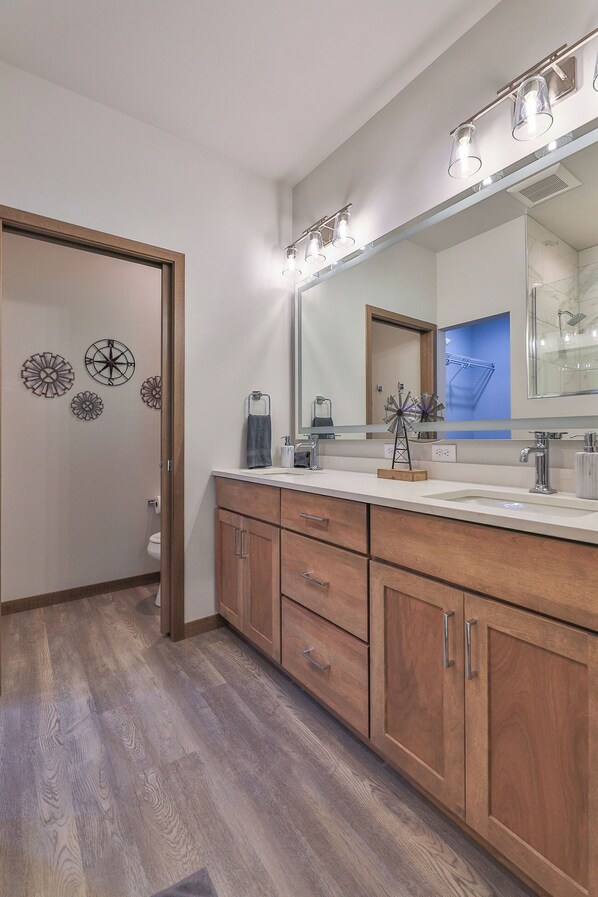 A modern bathroom with a large mirror, wooden cabinets, and a shower area.