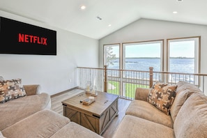 A living room with a large window overlooking a body of water, a wooden coffee table, and a couch with patterned cushions. - Lakefront 5BR on Rush Lake, Private Dock + Kayaks (New York Mills)