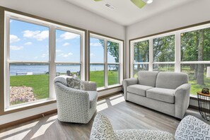 Una habitación con ventanas amplias, un sofá gris, sillones estampados y vistas a un lago.