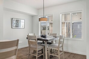 A dining area with a table and chairs, a hanging light fixture, and windows with blinds. - King Bed | Close to Airport | 6 Guests (Calgary)