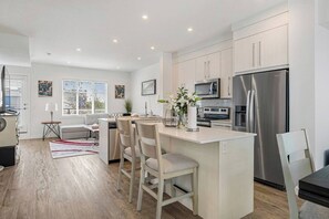 A modern kitchen with a central island, stainless steel appliances, and a dining area with chairs. - King Bed | Close to Airport | 6 Guests (Calgary)
