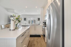 A modern kitchen with a stainless steel refrigerator, wooden cabinets, and a white countertop. - King Bed | Close to Airport | 6 Guests (Calgary)