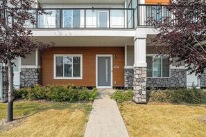 A two-story residential building with a stone facade, a wooden front door, and a visible address number. - King Bed | Close to Airport | 6 Guests (Calgary)