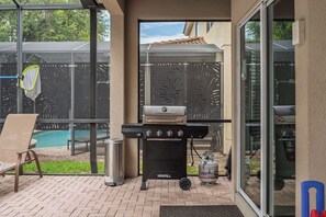 A patio with a grill, a pool, and a chair. - Themed House with Heated Private Pool & Game Room (Kissimmee)